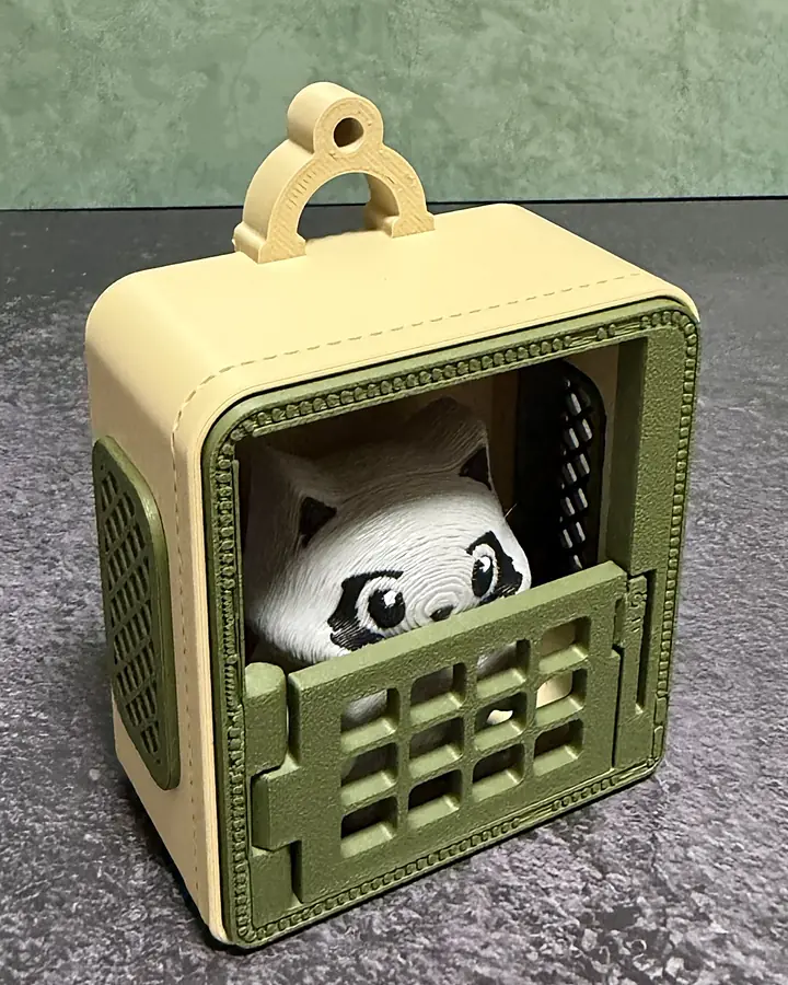 The sage carrier keychain from a three-quarter angle: cream body, sage-green door, grate, and lattice side panel, with the Raccoon inside